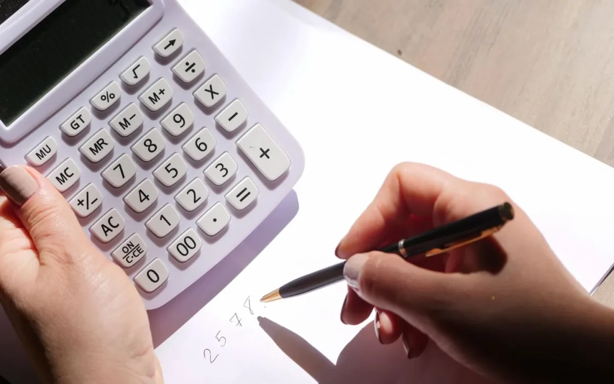 Mâini cu calculator și pix deasupra unei foi albe