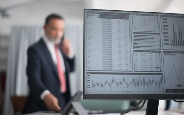 Monitor cu date și grafice financiare, lângă un bărbat