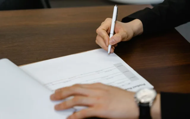 Persoană completând un document cu pixul la masă