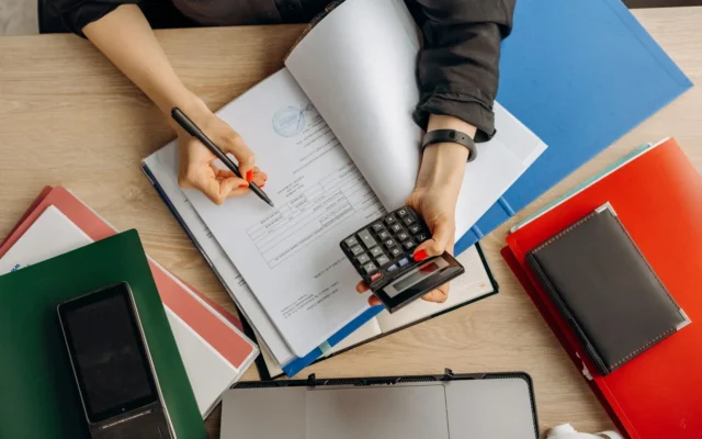 Mâini cu un calculator și documente pe birou