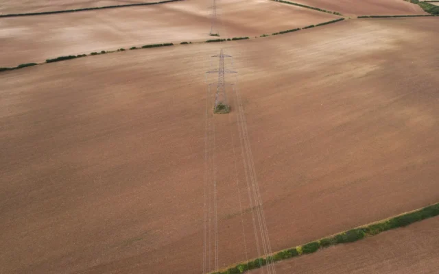 Stâlpi metalici și linii electrice deasupra unor câmpuri agricole